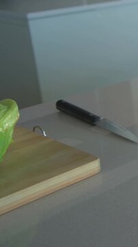 Vertical video: Panning camera showing lettuce wedge on board on counter with onion tomatoes knife