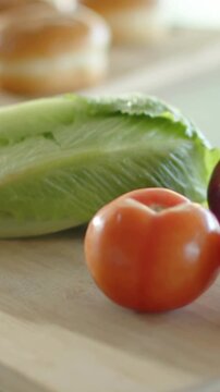 Vertical video: Racking focus camera shifting from tomato to buns, romaine on wood board for prep