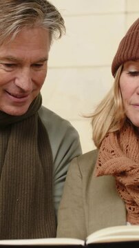 Vertical video: Looking down couple in scarves reading and turning pages to review book at bench
