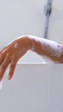 Vertical video: Making small downward moves, forearm sliding at tub rim, rinsing near chrome faucet