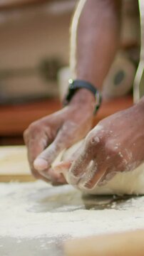 Vertical video: Starting closeup baker hands in apron pressing dough on counter to form boule, jar