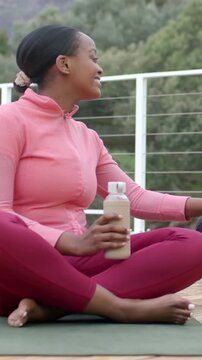 Vertical video: Hearing call woman in pink top turning reaching right on deck with mat and bottle