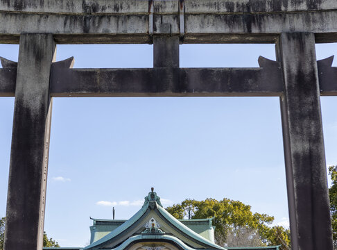 View of a traditional stone torii gate framing a shinto shrine roof under a clear blue sky in Osaka, Osaka, Japan.