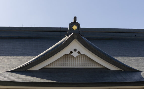 View of the ornate roof gable of a traditional Japanese building featuring dark tiles and a golden crest under a clear blue sky in Osaka, Osaka, Japan.