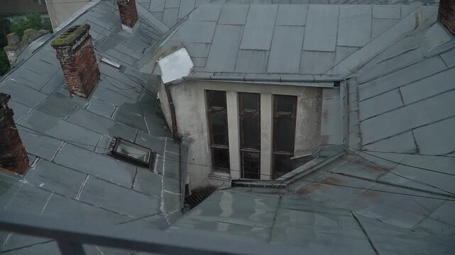 A view of the roof of an old architectural building with a hidden window, brick chimneys, slate, and tiles. A walk through the old part of the tourist town.