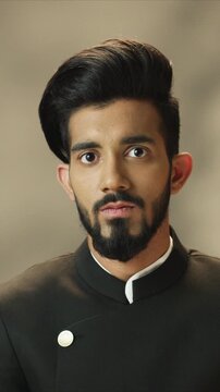 Serious close up portrait of handsome Arabian man wearing dark traditional jacket and looking straight at camera. Male standing calmly and expressing confidence. Indoor minimal lifestyle scene.