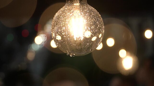 Raindrops falling on a garland bulb, the wind moves it, close-up shot, aesthetic video, decor. blurred raindrops, bokeh of warm incandescent lights