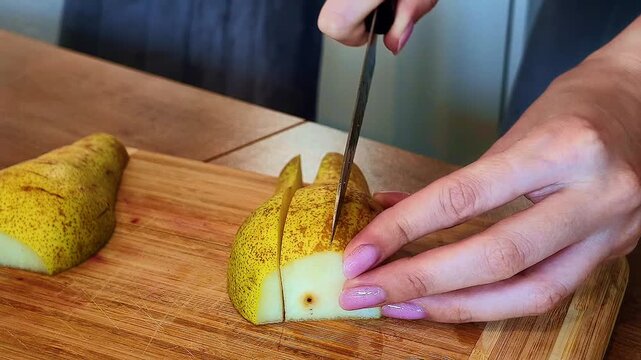 Close-up: slicing a pear into thin pieces with a kitchen knife on a cutting board.