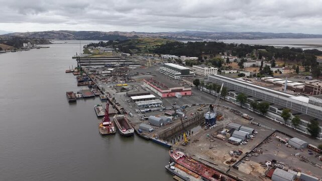 VALLEJO, CALIFORNIA, USA - JUNE 19, 2026: Aerial view of the working waterfront at the historic Mare Island shipyard, with finger piers, a moored vessel, cranes, a laydown yard and warehouses.