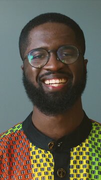 Serious close up portrait African American man wearing glasses and patterned shirt looking at camera and smiling. Male standing still and expressing confidence and happiness. Indoor studio scene.