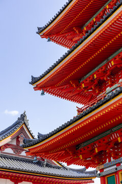 View of the vibrant red wooden eaves and dark tiled roofs of a traditional Japanese temple against a clear blue sky in Kyoto, Kyoto, Japan.