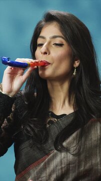 Festive close up portrait beautiful woman holding party horn and blowing celebration sound. Female enjoying holiday moment and making noise. At home. Indoor cultural lifestyle scene. Celebration.