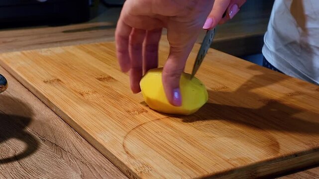Close-up: slicing a potato into thin slices with a kitchen knife on a cutting board.
