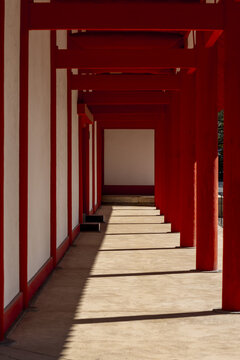 View of a traditional vermilion shrine corridor with red wooden pillars and white walls casting long shadows on the floor in Kyoto, Kyoto, Japan.