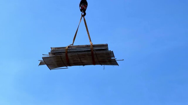 Construction material bundle lifted by crane against blue sky