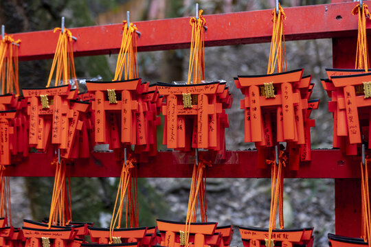View of small orange torii gate votive tablets with handwritten messages hanging on a red wooden rack at the Senbon Torii in Kyoto, Kyoto, Japan.