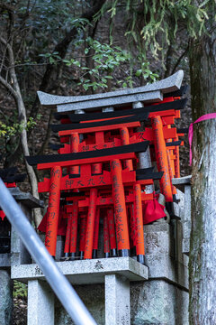 View of small red torii gates with black tops and Japanese inscriptions stacked on a stone pedestal in a wooded area at Senbon Torii Kyoto, Kyoto, Japan.