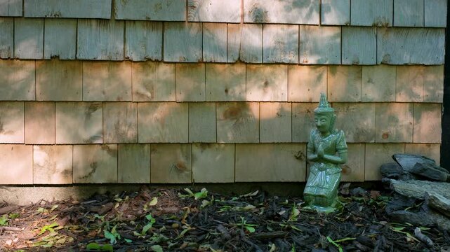 Branch shadows shifting over a wooden shingle wall by a small statue