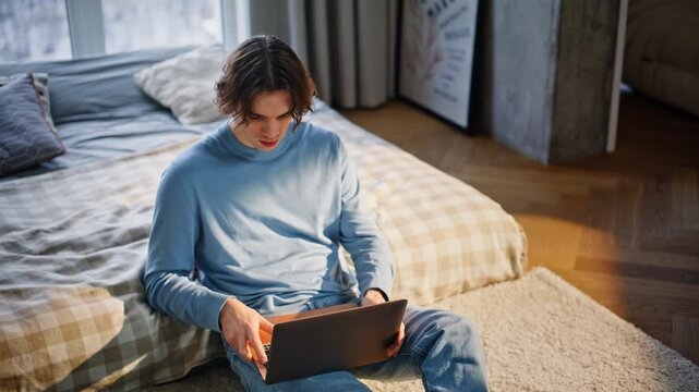 Domestic student texting essay using laptop sitting floor. Man typing computer