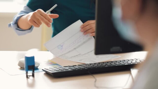 A doctor is typing on a document at a desk, using a computer in a well-lit office during the day