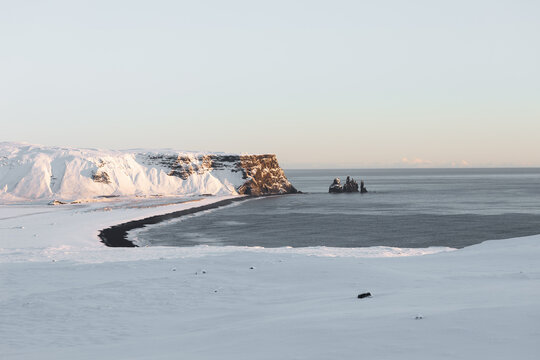 View of the snow-covered cliffs and Reynisdrangar sea stacks at the black sand beach in Iceland.