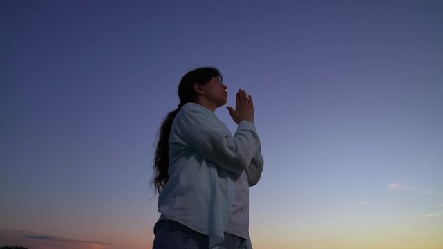 Relaxation, meditation, nature. Woman confessing. Christian woman praying sunset, close-up. Faith in God. Woman praying with family, children, sky, morning. Asking forgiveness. Hope. People of