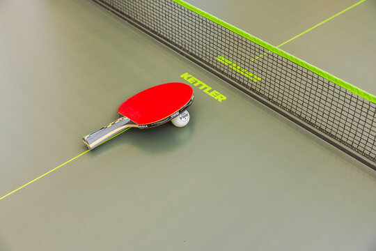 Close-up view of Kettler table tennis paddle and ball resting beside net on outdoor ping pong table. Sweden. 