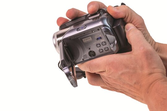 Close-up view of hands operating JVC digital camcorder with flip screen and Dolby Digital logo isolated on white background. Sweden.