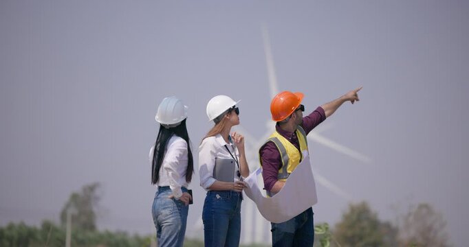 Team of engineers reviewing wind farm plans discussing renewable energy project at turbine site