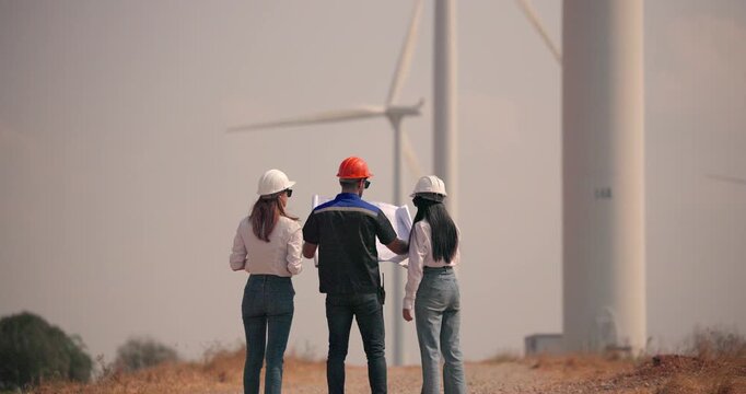 Team of engineers reviewing wind farm plans discussing renewable energy project at turbine site