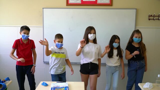 Group of school children in masks waving hands then taking off face masks in school corridor, back to normal education concept stock video.