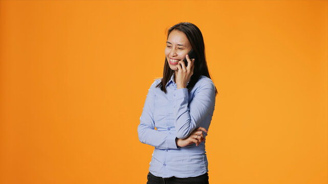 Casual adult receiving phone call in front of camera, chatting with friends on smartphone telecommunications network, Asian girl answering telephone for remote discussion in studio.