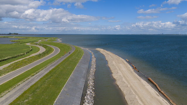 Aerial view of the dike reinforcement project along the coastline with a winding road, green embankments, and sandy construction works in Uitdam, North Holland, Netherlands.