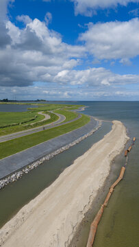 Aerial view of the dike reinforcement project along the coastline with a winding road, green embankments, and sandy construction works in Uitdam, North Holland, Netherlands.