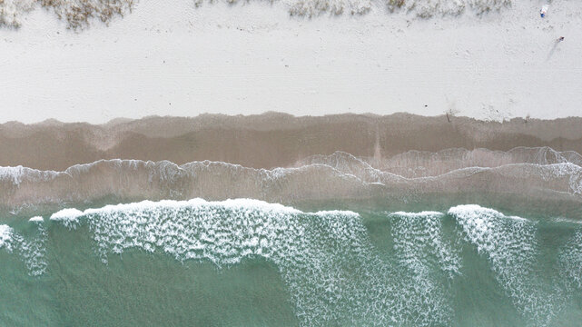 Aerial view of the sandy shoreline and turquoise waves crashing on Omaha Beach, Omaha, Auckland, New Zealand.