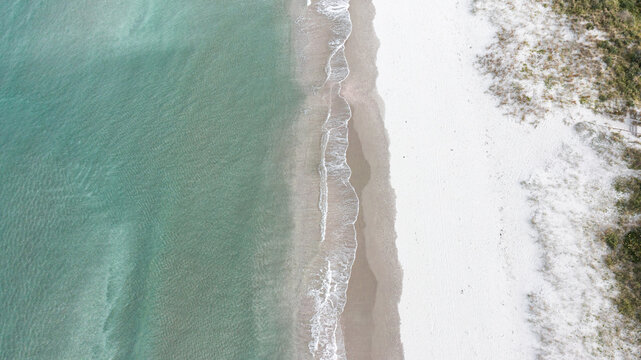 Aerial view of the white sand beach and turquoise water at Omaha Beach with gentle waves lapping the shore in Omaha, Auckland, New Zealand.