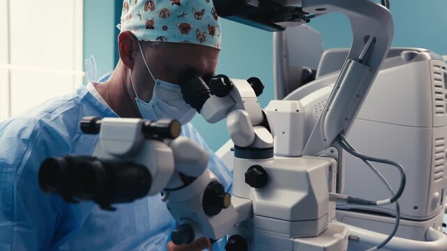 Male ophthalmic surgeon in blue scrubs uses a surgical microscope for precise examination, focused on patient care in a bright medical environment