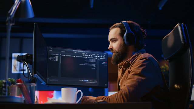 Cheerful programmer listening music while doing web development during remote job shift in neon lit home office, finishing coding project, iT expert enjoying audio podcast, working on PC.