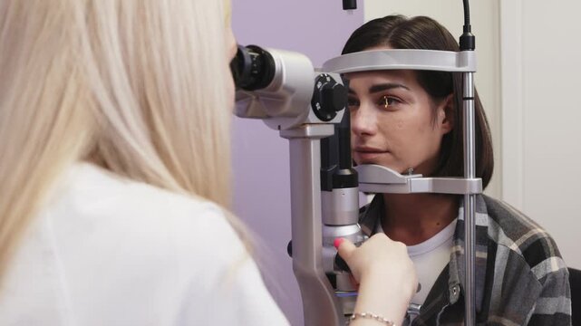 Female optometrist examines patient's eye using slit lamp, focusing on eye illumination and detailed observation in a clinical setting with medical equipment