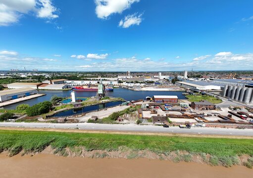 Aerial view of the industrial port and canal in Goole with cargo ships, warehouses, and storage silos under a bright blue sky in Goole, England, United Kingdom.
