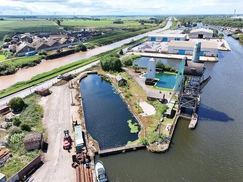 Aerial view of the historic industrial docks and canal infrastructure with a prominent crane, warehouses, and surrounding green fields in Goole, England, United Kingdom.