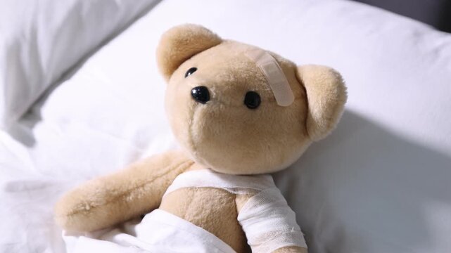 Pediatrician concept. Toy bear with bandage in bed, closeup