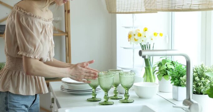Happy young woman with clean plates and glasses at counter in kitchen