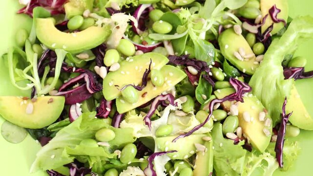 Delicious salad with avocado, beans and greens as background, top view
