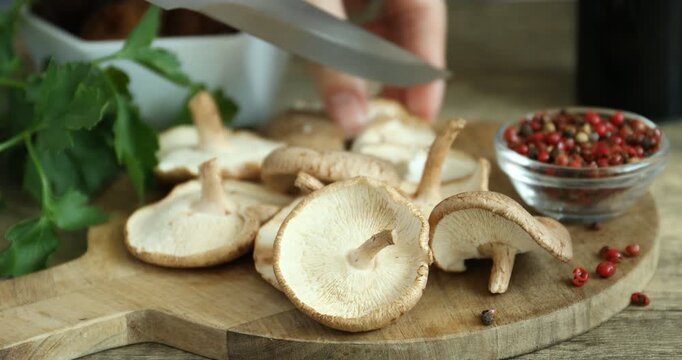 Woman cutting raw shiitake mushrooms at wooden tiled table, closeup