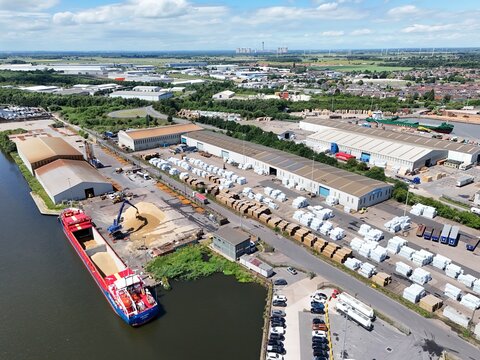 Aerial view of the industrial port featuring a cargo ship being loaded with grain, warehouses, and stacks of white-wrapped materials in Goole, England, United Kingdom.