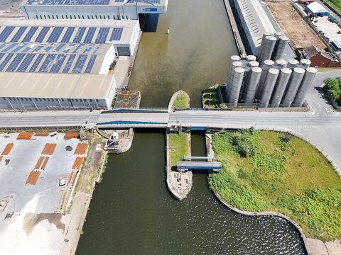 Aerial view of the canal lock system featuring industrial warehouses with solar panels on rooftops, large storage silos, and surrounding green spaces in Goole, England, United Kingdom.