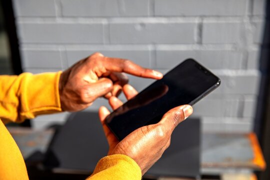 Person in yellow sweater using a smartphone outdoors.