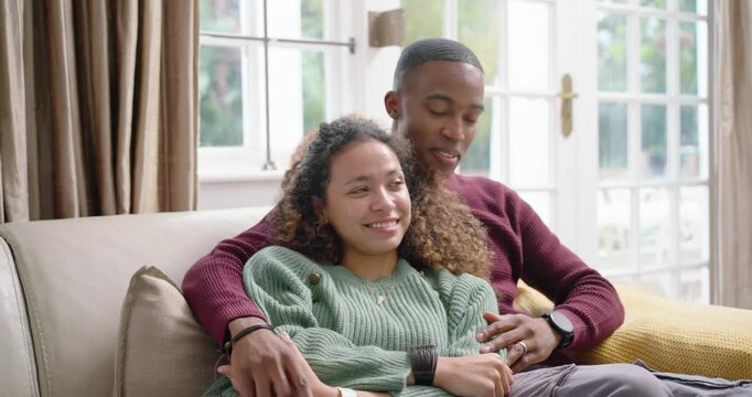 Couple sitting on sofa near French doors, woman leaning back as man wrapping arms while talking