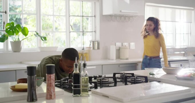 Diverse couple in home kitchen, woman entering, man holding roasting pan checking roast on gas hob